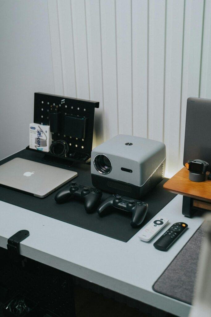 A sleek home office setup featuring a projector, game controllers, and laptop.